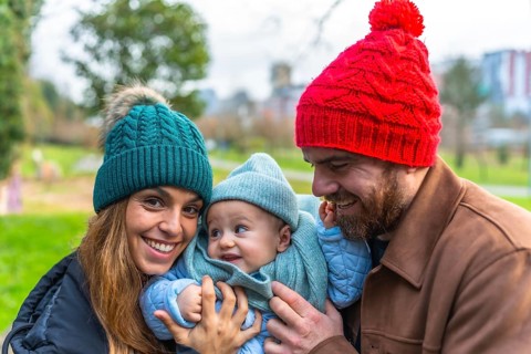 Smiling parents holding their baby, enjoying a joyful winter day together at the park, creating
