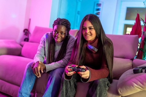 Two friends enjoying their free time playing with a gamepad sitting on a sofa in a colorful living
