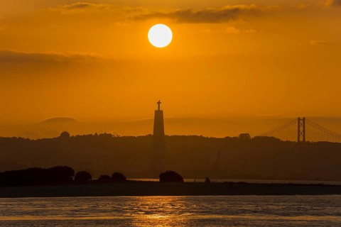 Atmospheric scene with a sunset over a statue and a bridge bathing the water in golden light,