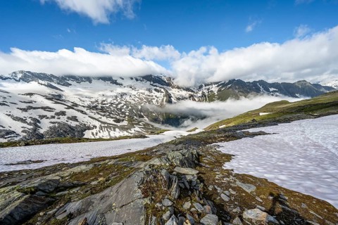 Mountain landscape with snowfields and high fog in the valley, behind summit Hoher Weißzint and