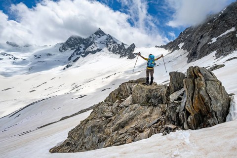 Mountaineer on a rock between snow, raises her arms triumphantly, descending from the summit of