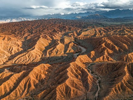River bed runs through a landscape of eroded hills, badlands at sunset, mountain peaks of the Tian