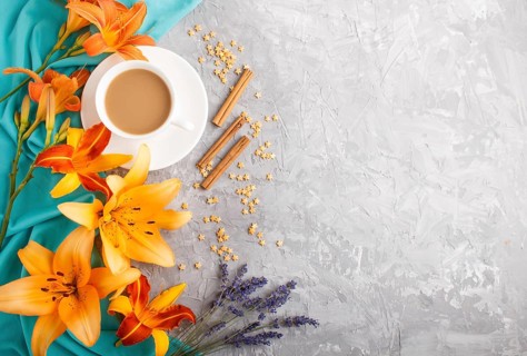 Orange day-lily and lavender flowers and a cup of coffee on a gray concrete background, with blue