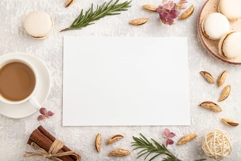 White paper sheet mockup with cup of coffee, almonds and macaroons on gray concrete background.