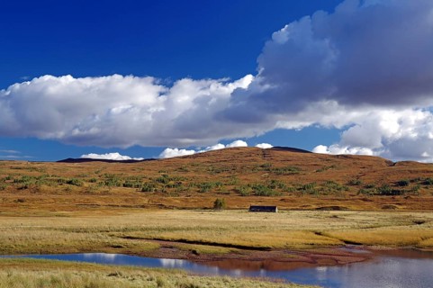 Peaceful lake surrounded by meadows and hills under a blue sky with white clouds, autumn, October,