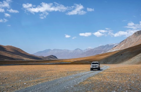 Off-road vehicle on gravel track, Burkhan mountain valley with meandering river, barren dramatic