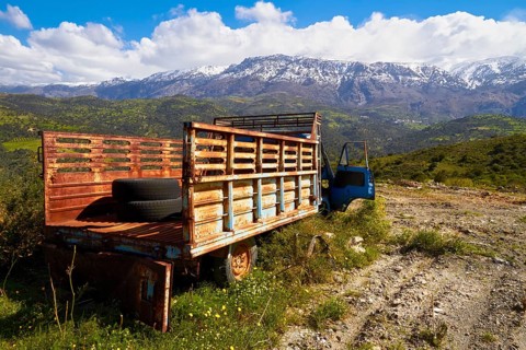 Abandoned rusted lorry in a sunny mountain landscape with snow-capped peaks, wrecked vehicle,