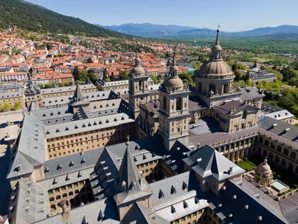 Close-up of a historic monastery with towers, surrounded by a town and mountains in the background,