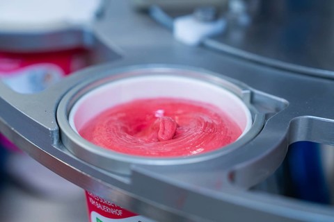 Raspberry ice cream in a cup during the filling process, ice cream production farm ice cream,