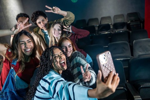 Group of cheerful young friends taking selfie at movie theater or disco party, making victory signs