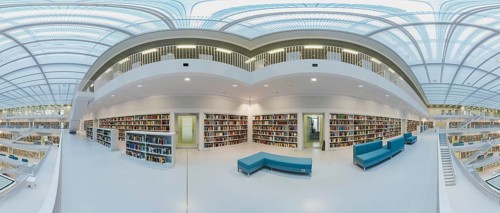 Modern library with glass roof and white stairs, surrounded by bookshelves in a bright open space,