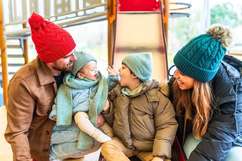Happy family dressed in warm winter clothing enjoying playful moments together on a playground