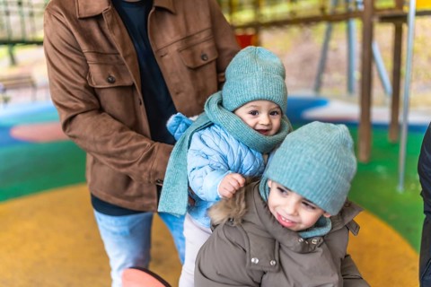 Father holding two joyful children in colorful winter clothes while enjoying playful moments at an