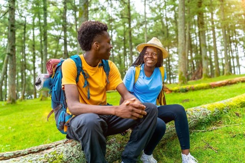 Two male and female african friends resting and chatting during a hiking in the forest