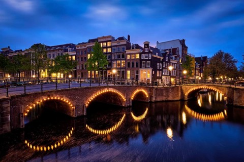 Night view of Amsterdam cityscape with canal, bridge and medieval houses in the evening twilight