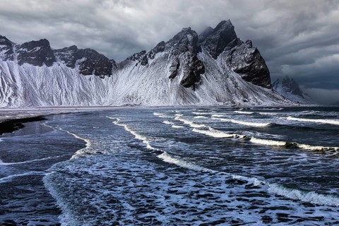 White foamy waves on the beach of Stokkness, behind snowy rocky slopes of Vestrahorn, near Höfn,