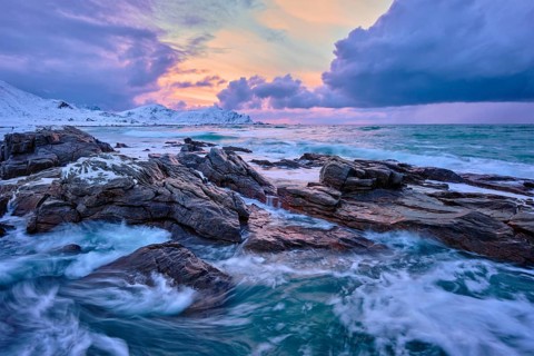 Waves of Norwegian sea on rocky coast in fjord on sunset with sun. Skagsanden beach, Lofoten