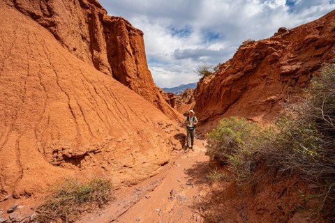 Mountaineers in a canyon with a dry stream bed, eroded mountain landscape with red sandstone rocks,
