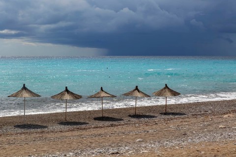 Line of sunshades along the beach with dark storm clouds offshore, Dhermi, Albania, Europe