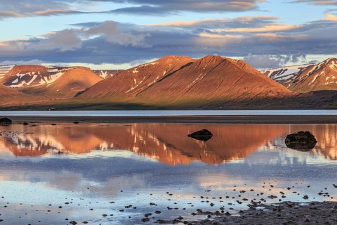 Fjord, low tide, stones, mountains reflected in the water, evening light, cloudy mood, Thingeyri,