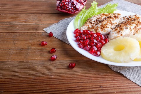 Fried chicken fillets with lettuce, pineapple and pomegranate seeds on brown wooden background,