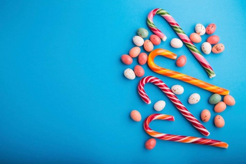Colorful multicolored candies on a blue background. Christmas cane, chocolate eggs, caramel dragees