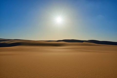 The endless expanse of a desert with golden sand dunes under a bright blue sky and the glistening
