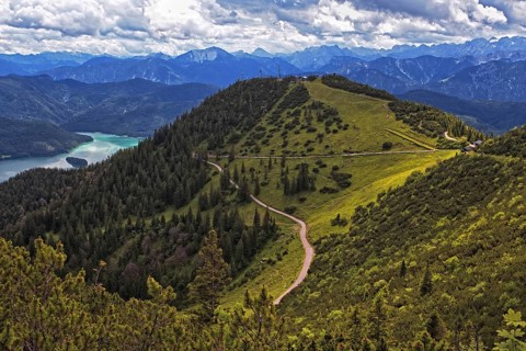 Panoramic view from the Herzogstand of wooded mountains and a winding hiking trail, with Lake