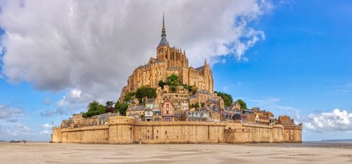 Impressive abbey on an island in the middle of a vast sandy landscape under a blue sky, Le