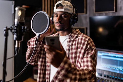 Young man recording vocals for new hit album in professional music studio, using pop filter and