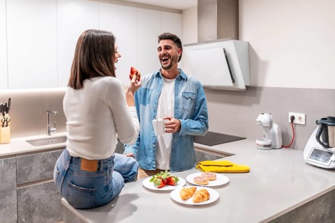 Young couple sharing a lighthearted breakfast in their contemporary kitchen, enjoying strawberries,