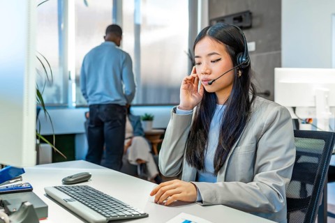 Asian customer service representative working with headset and computer in bright coworking office