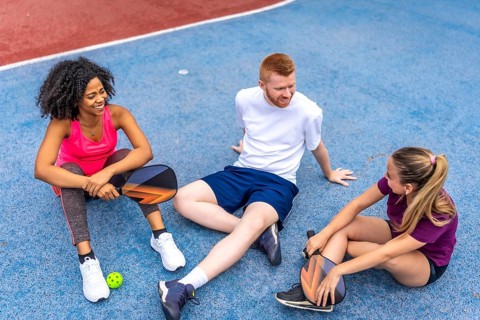 Multi-ethnic friends sitting on the ground relaxed and talking in a pickelball court