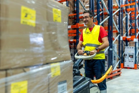 Mature happy man working in a warehouse moving boxes with forklift