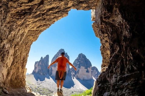 Hiker enjoying the breathtaking view of the tre cime di lavaredo from inside a Tre Cime Cave in the