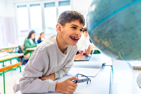 Happy student with down syndrome smiling while exploring a globe in geography class, showcasing