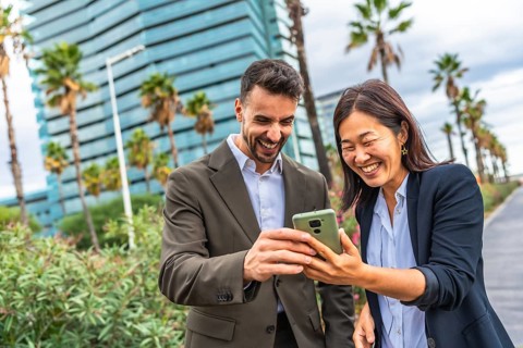 Chinese and caucasian business people laughing while looking at the mobile in the city
