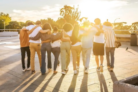Rear view of friends embracing walking together along the city during sunset