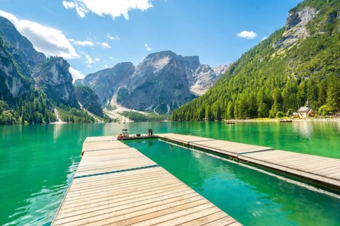 Wooden pier reflecting in the emerald waters of lake braies, surrounded by the dolomites on a sunny