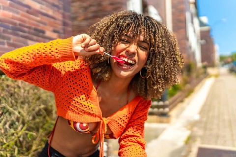 Cute and beauty young latin woman biting a heart shaped lollipop in the street