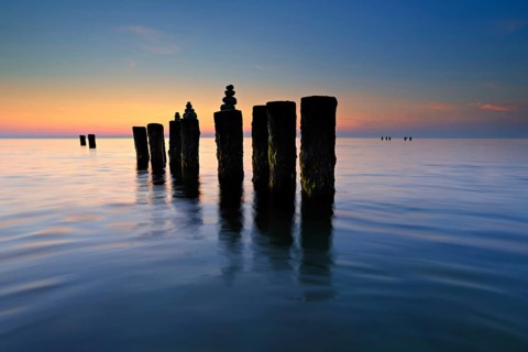 Stone pyramids on old groynes with algae in the water on the Baltic Sea beach at sunset, Wustrow,