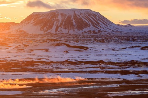 Hot springs and geothermal area in front of mountain landscape in winter, sunbeams, cloudy mood,