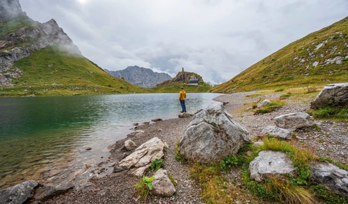 Mountaineer in yellow jacket at the mountain lake, view over the Wolayersee lake to the alpine club