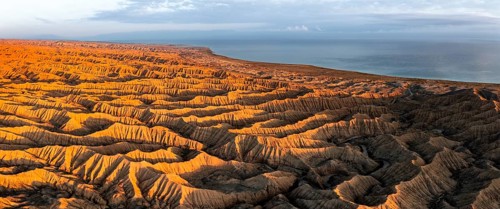 Landscape of eroded hills, badlands at sunset, Lake Issyk Kul in the background, aerial view,