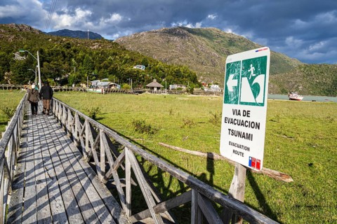 Signpost showing evacuation route in case of a tsunami, wooden boardwalk of Caleta Tortel, Aysen