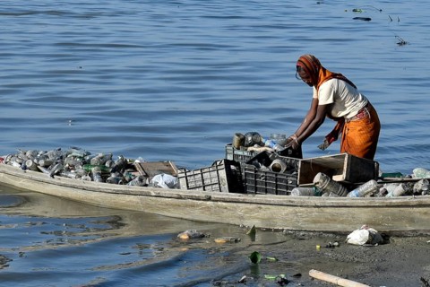 A women rag picker collecting plastic bottle and other plastic materials in a boat from the bank of