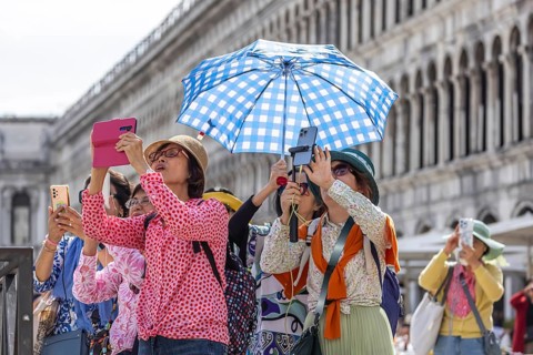 Tourists from Asia with mobile phones and parasols taking photos. Souvenir photo of St Mark's