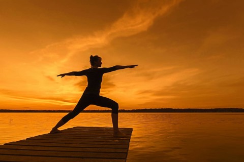 Woman practicing yoga posture Virabhadrasana II, Warrior Pose, lunging standing asana on jetty at