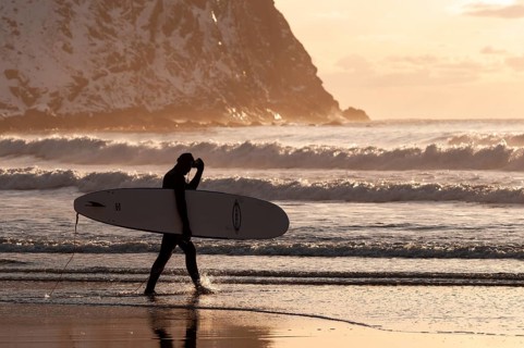 Surfer with surfboard under his arm on the beach of Unnstad, winter surfing, Lofoten Island