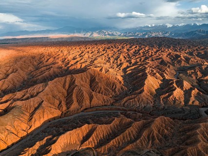 River bed runs through a landscape of eroded hills, badlands at sunset, mountain peaks of the Tian